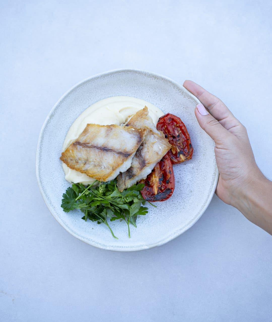 Prato com filé de peixe grelhado sobre purê de batata, tomates assados e salsinha.